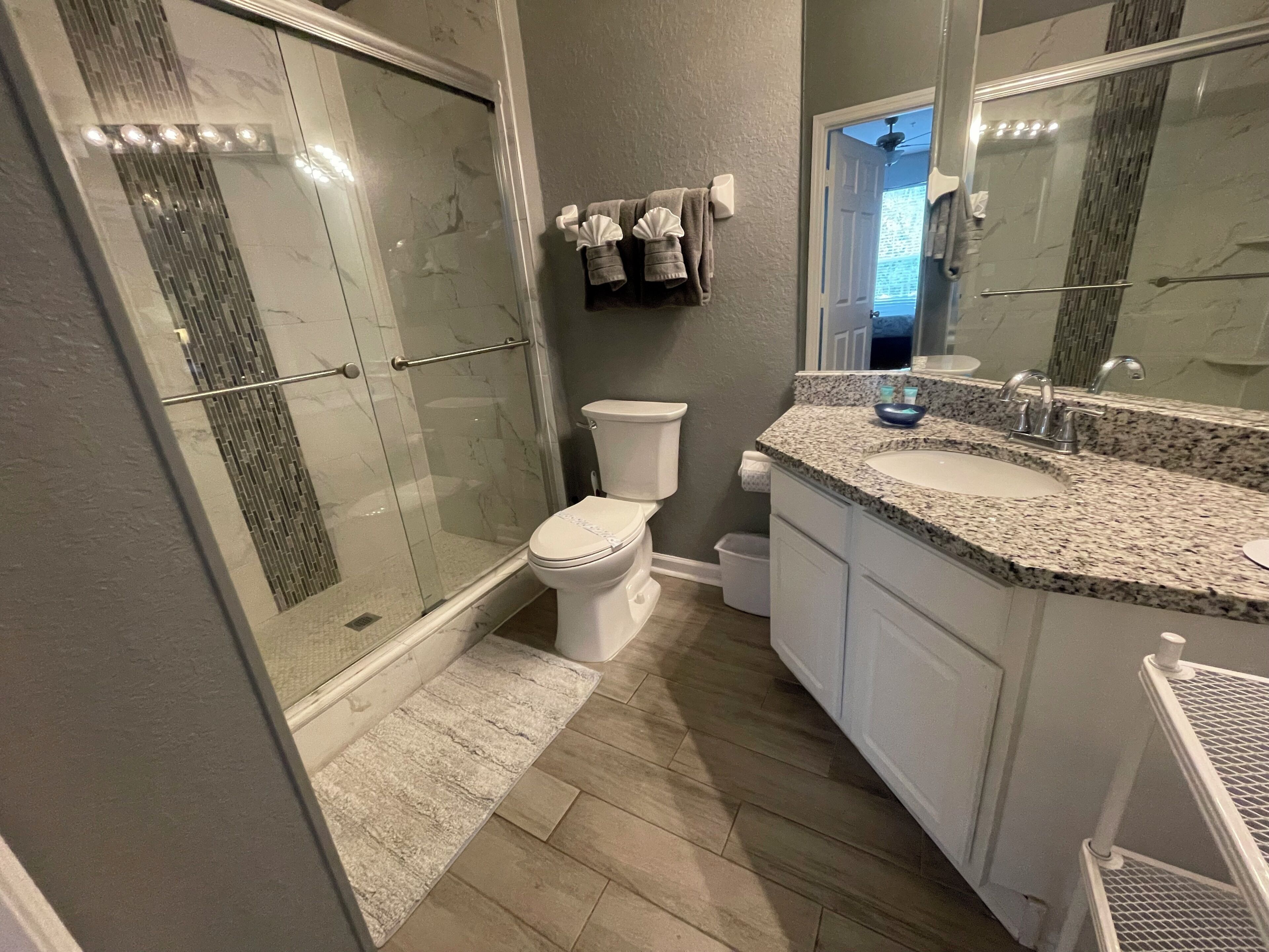 A bathroom with a glass-enclosed shower, a toilet, a sink with a granite countertop, and a large mirror.