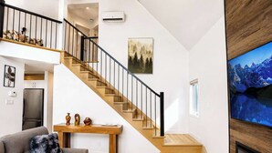 Una sala moderna con una escalera, un televisor de pantalla plana y una chimenea.