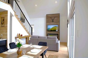 Ein modernes Wohnzimmer mit Essbereich, einer Treppe und einem Wand-Fernseher.