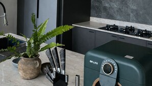 Una cocina moderna con un refrigerador negro, armarios de madera, una estufa a gas y lámparas colgantes de mimbre.