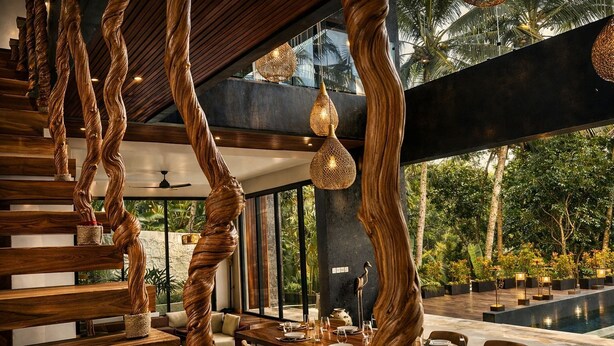 Un comedor moderno con escalera de madera, luces colgantes y vistas al exterior.