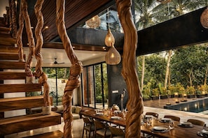 Un comedor moderno con escalera de madera, luces colgantes y vistas al exterior.