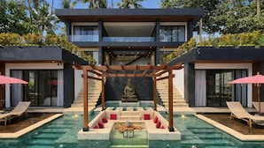 Un resort moderno con una piscina central, una estatua de Buda y una escalera que conduce a los niveles superiores.