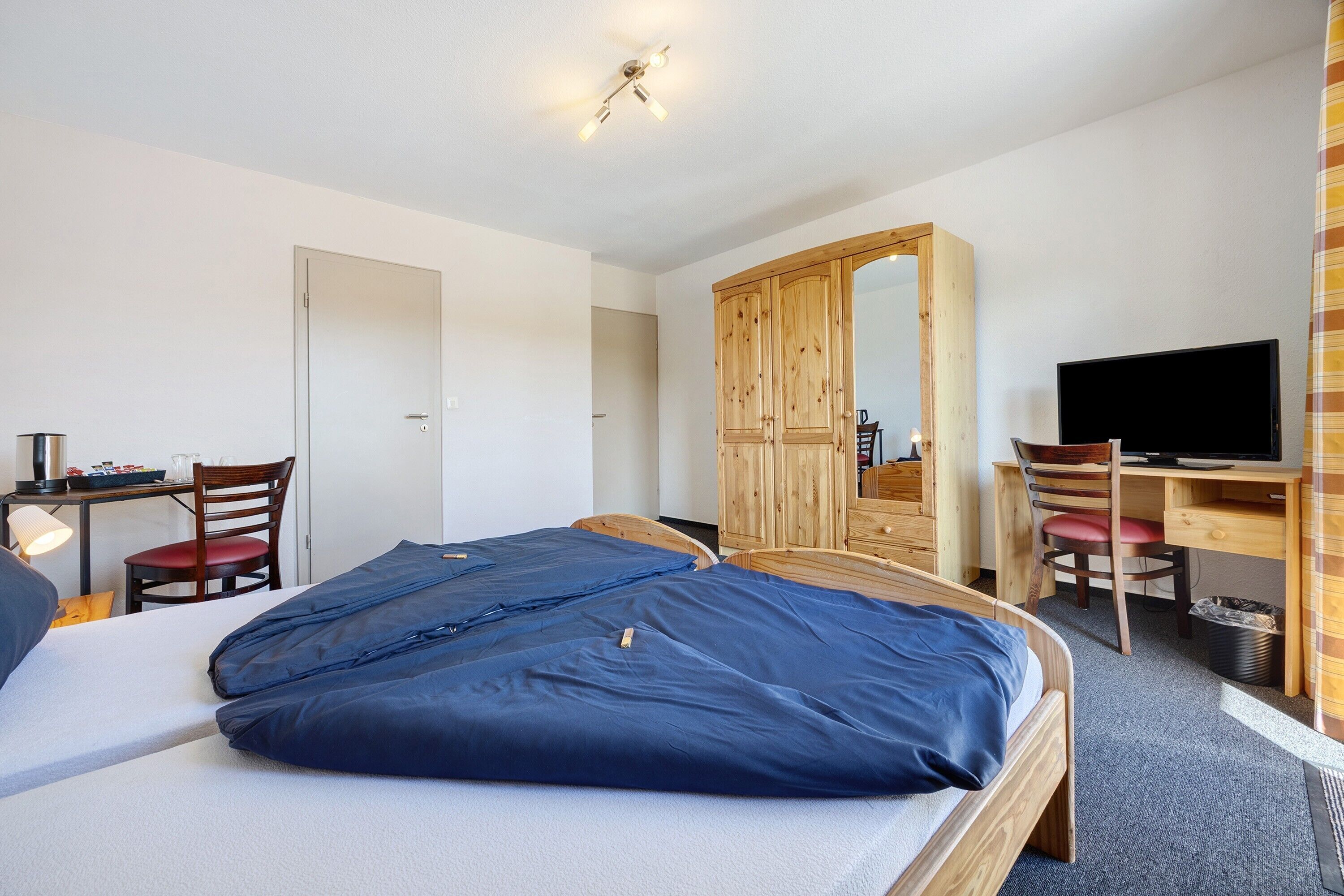 A bedroom with a bed, a desk, a chair, a television, and a wardrobe.