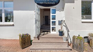 A building entrance with a sign reading 'ESSKAPADE zum Hackemack,' a wooden bench with flowers, and a potted plant. - Room 3 with Balcony for 2 Guests (Extertal)