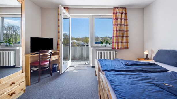 A bedroom with a bed, a desk with a chair, a TV, and a window with curtains. - Room 3 with Balcony for 2 Guests (Extertal)