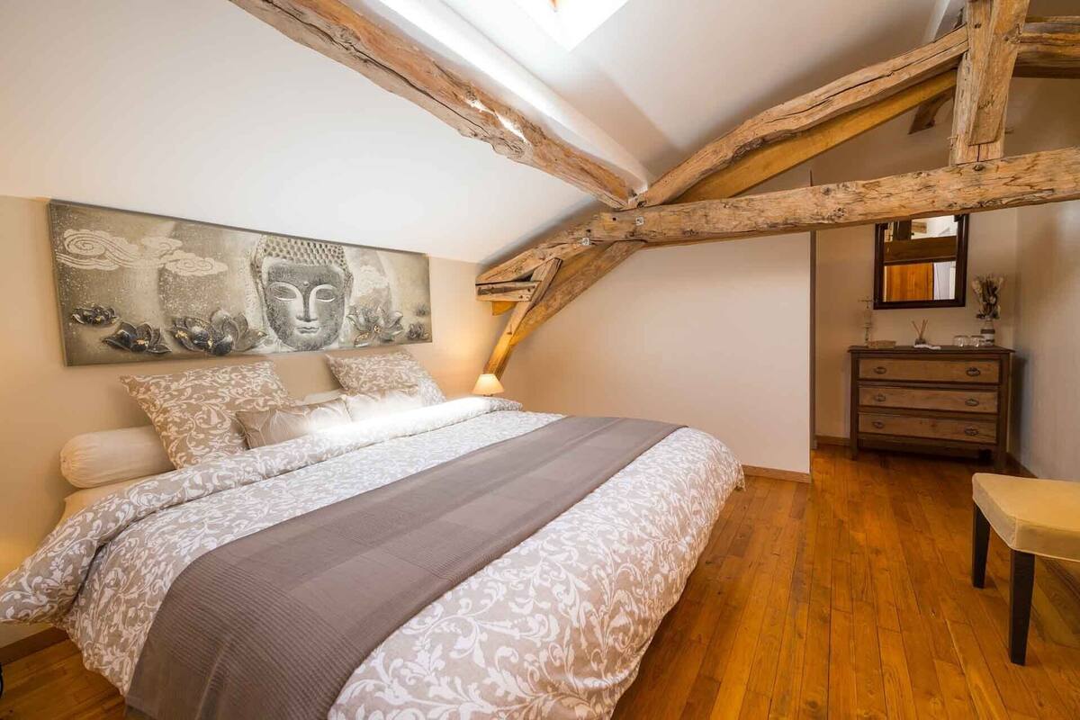 Ein Schlafzimmer mit einem großen Bett, Holzbalken, einem Schminktisch und einem Buddha-Gemälde.
