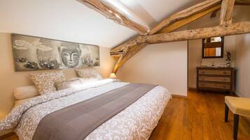 Een slaapkamer met een groot bed, houten balken, een dressoir en een Boeddha-schilderij.
