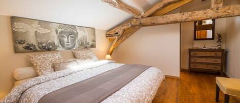A bedroom with a large bed, wooden beams, a dresser, and a Buddha painting.