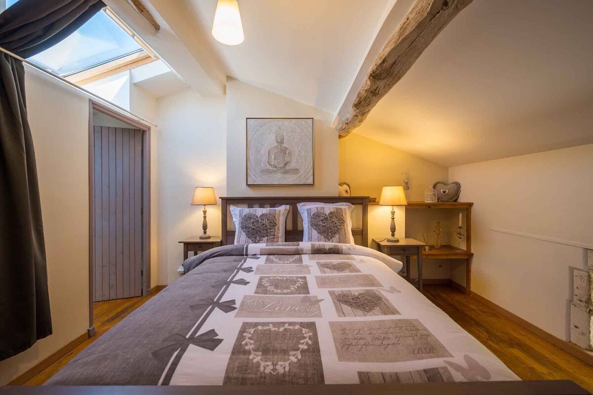 Ein Schlafzimmer mit einem Bett, zwei Nachttischen, einem Fenster, einem Oberlicht, einem Wandbild und einem Regal mit Dekoration.