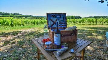 A picnic setup with a bottle, bread, cheese, and a basket on a wooden table in a vineyard.