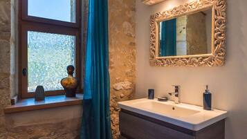 Une salle de bain avec un mur en pierre, une fenêtre offrant une belle vue, un miroir doté d’un cadre orné et un lavabo avec des accessoires modernes.