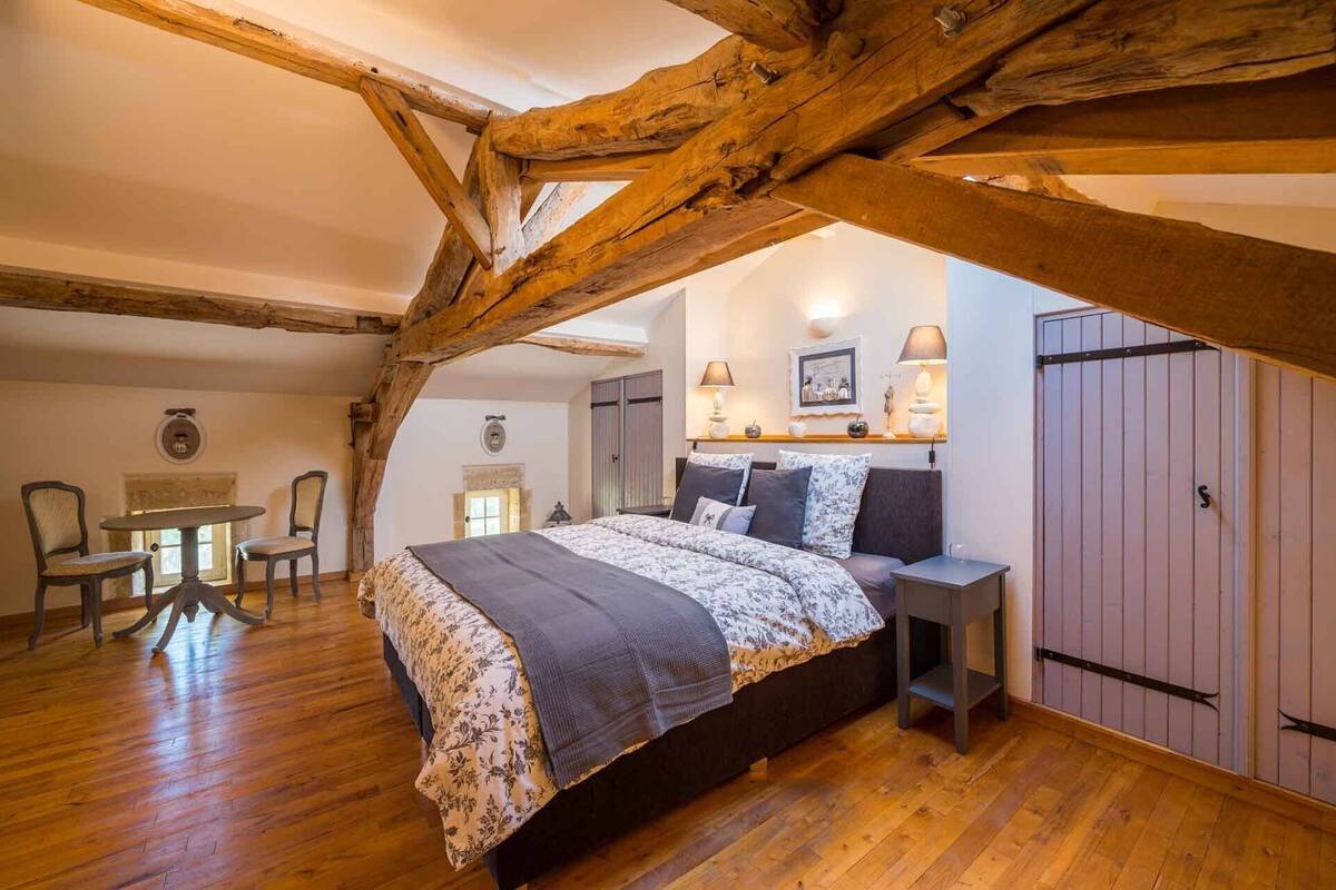 Ein Schlafzimmer mit Holzboden, einem Bett mit floralem Bettzeug, einem Nachttisch, einem Sessel und einem Kleiderschrank.
