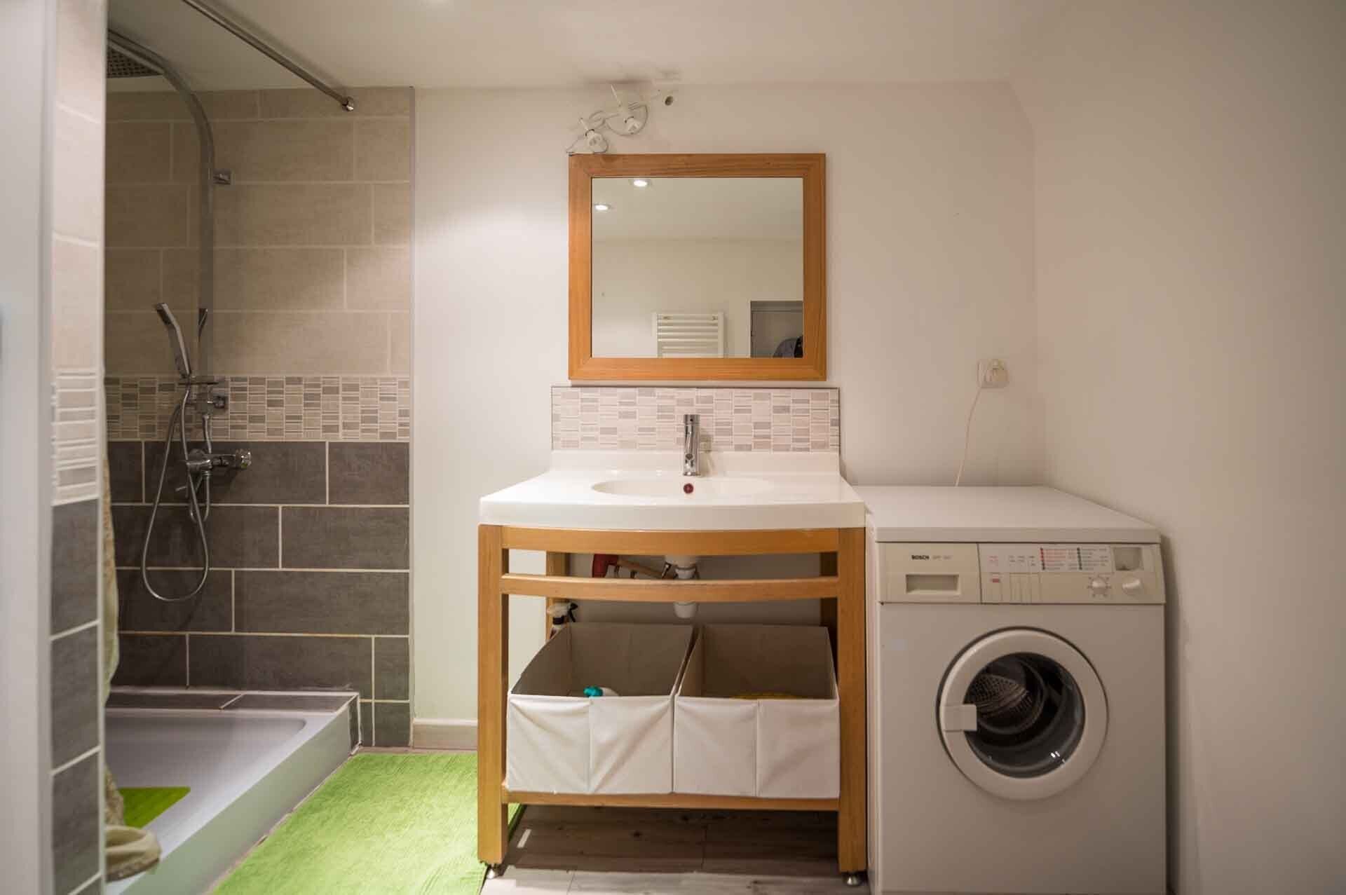 Ein Badezimmer mit Dusche, Waschbecken, Spiegel und Waschmaschine.