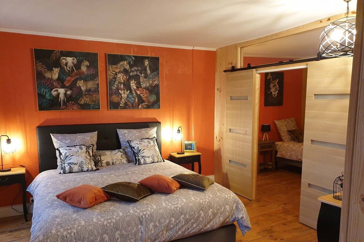 Ein Schlafzimmer mit einem Bett, zwei an der Wand befestigten Bildern, einem Nachttisch mit Lampe und einer Tür zu einem anderen Raum.