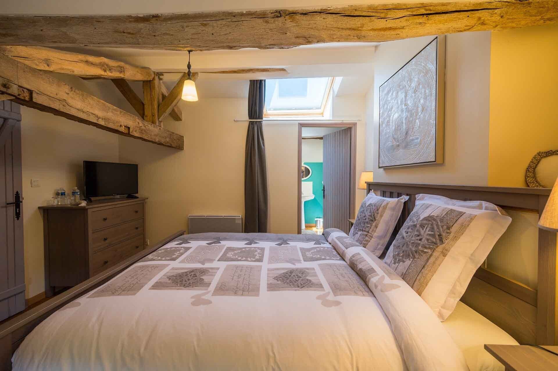 Een slaapkamer met een bed, een televisie, een dressoir, een dakraam en een schilderij aan de muur.