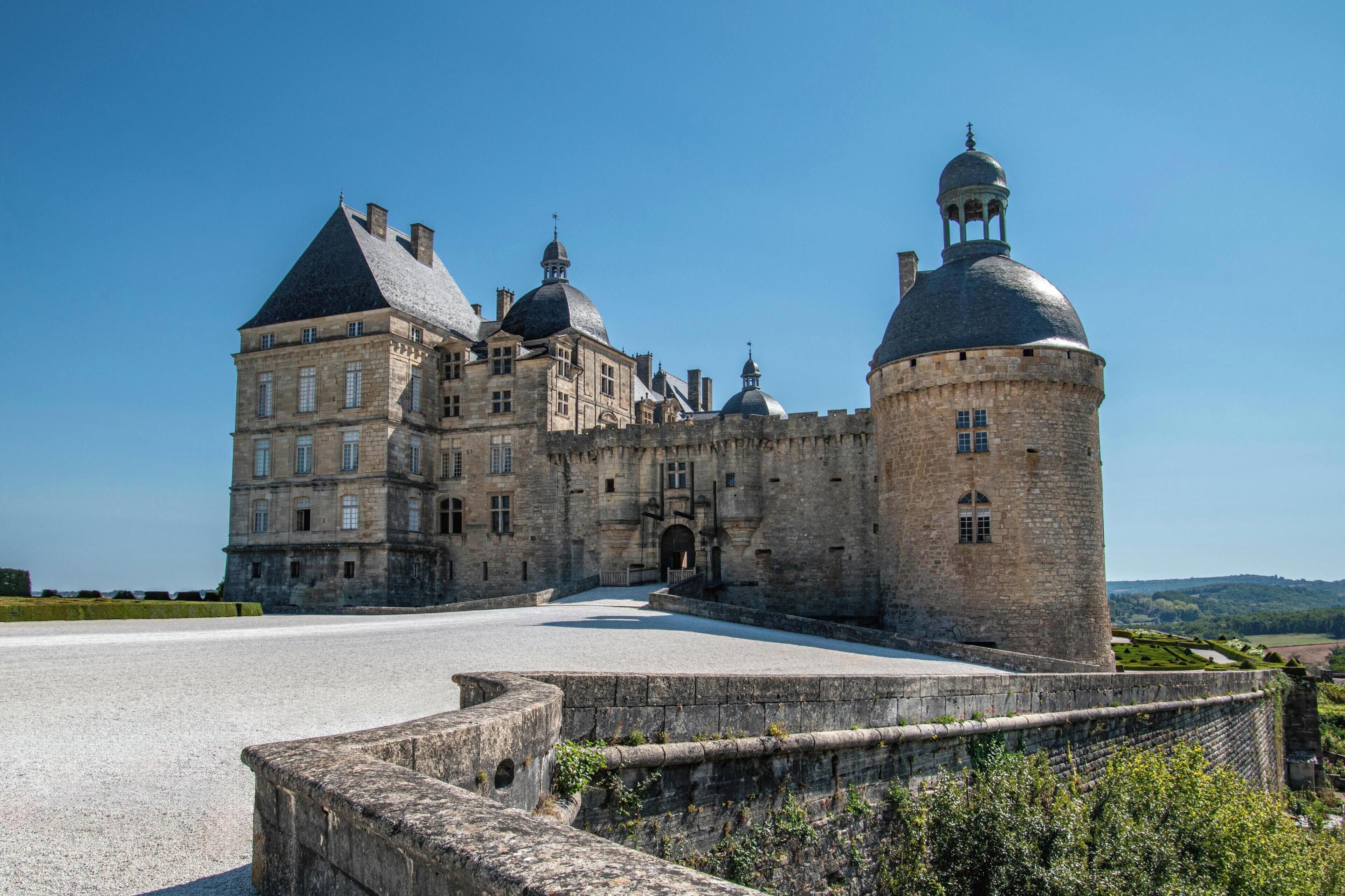 A historic castle with a large courtyard, a round tower, and a main building with multiple windows and a central entrance.