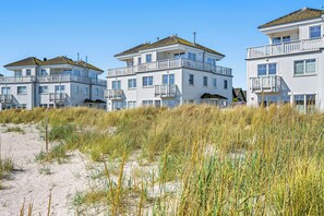 A beachfront hotel with multiple balconies and a sandy beach in the foreground. - The Beach House: beach villa with sauna, whirlpool and roof terrace in Olpenitz (Kappeln)