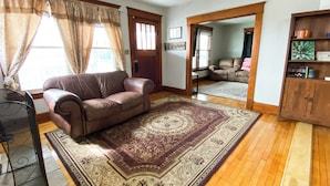 Un salon avec un canapé en cuir marron, un tapis à motifs, un parquet et un meuble en bois orné d’objets décoratifs.