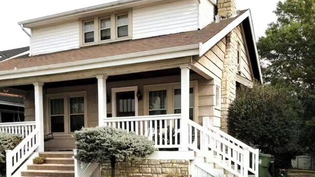 Une maison à deux étages avec un porche, une cheminée et des fondations en pierre.