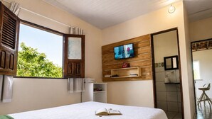 A bedroom with a bed, a TV mounted on the wall, a window with curtains, and a view of greenery outside. - Casa Vilar Rio Lençois Maranhenses (Barreirinhas)