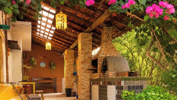 Ein Terrassenbereich im Freien mit Lehmofen, Holzbalken und hängenden Lichtern.