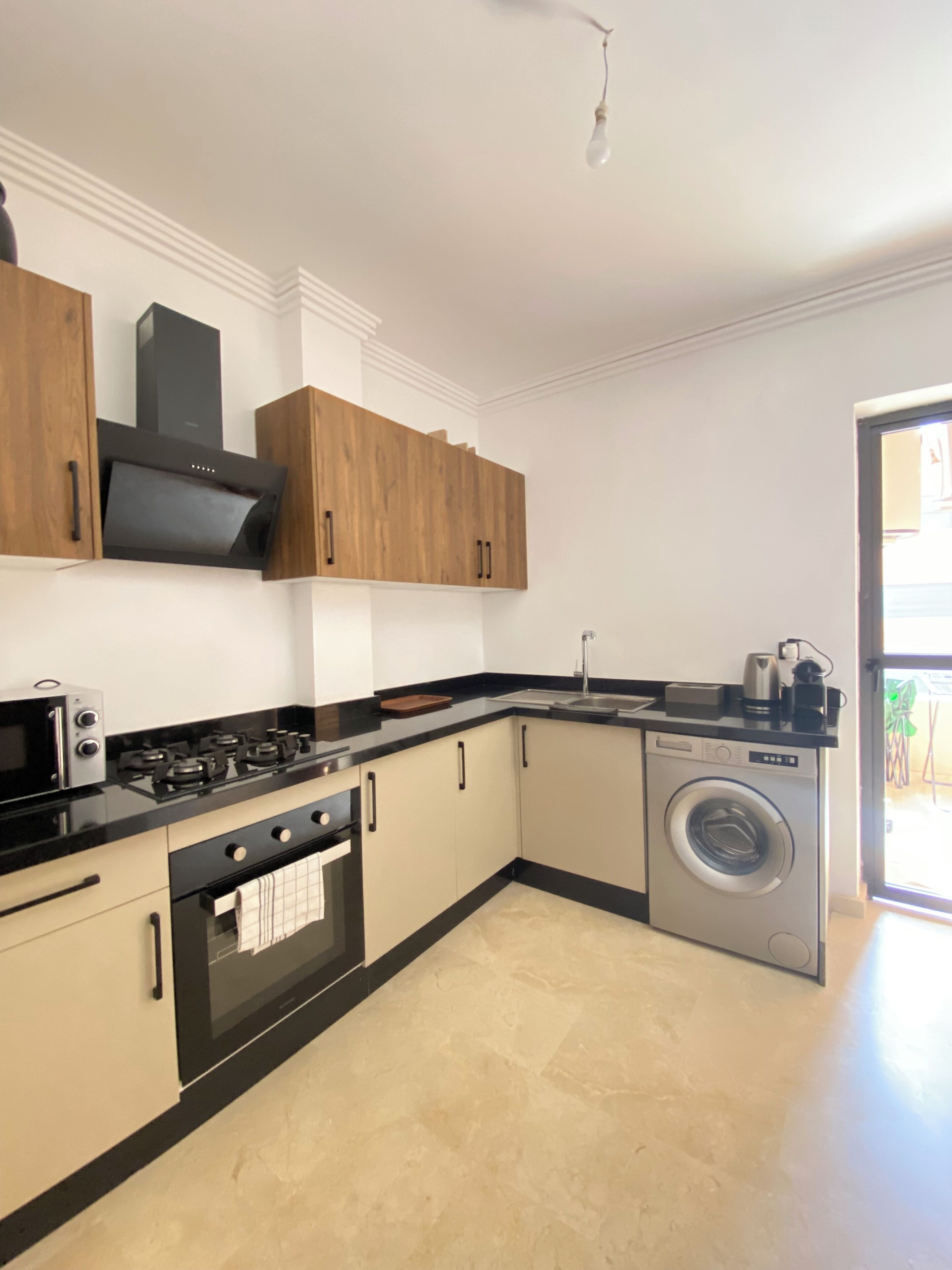 A modern kitchen with wooden cabinets, a built-in oven, a washing machine, and a black countertop.