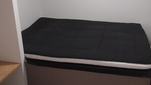 Een kleine eenpersoonskamer met een wit plafond, een wandairconditioner en een houten plank.