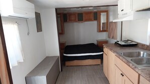 Een kleine keuken met een spoelbak, houten kastjes, een bed en een kleine koelkast.