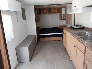 Eine kleine Küche mit Spüle, Holzschränken, einem Bett und einem kleinen Kühlschrank.