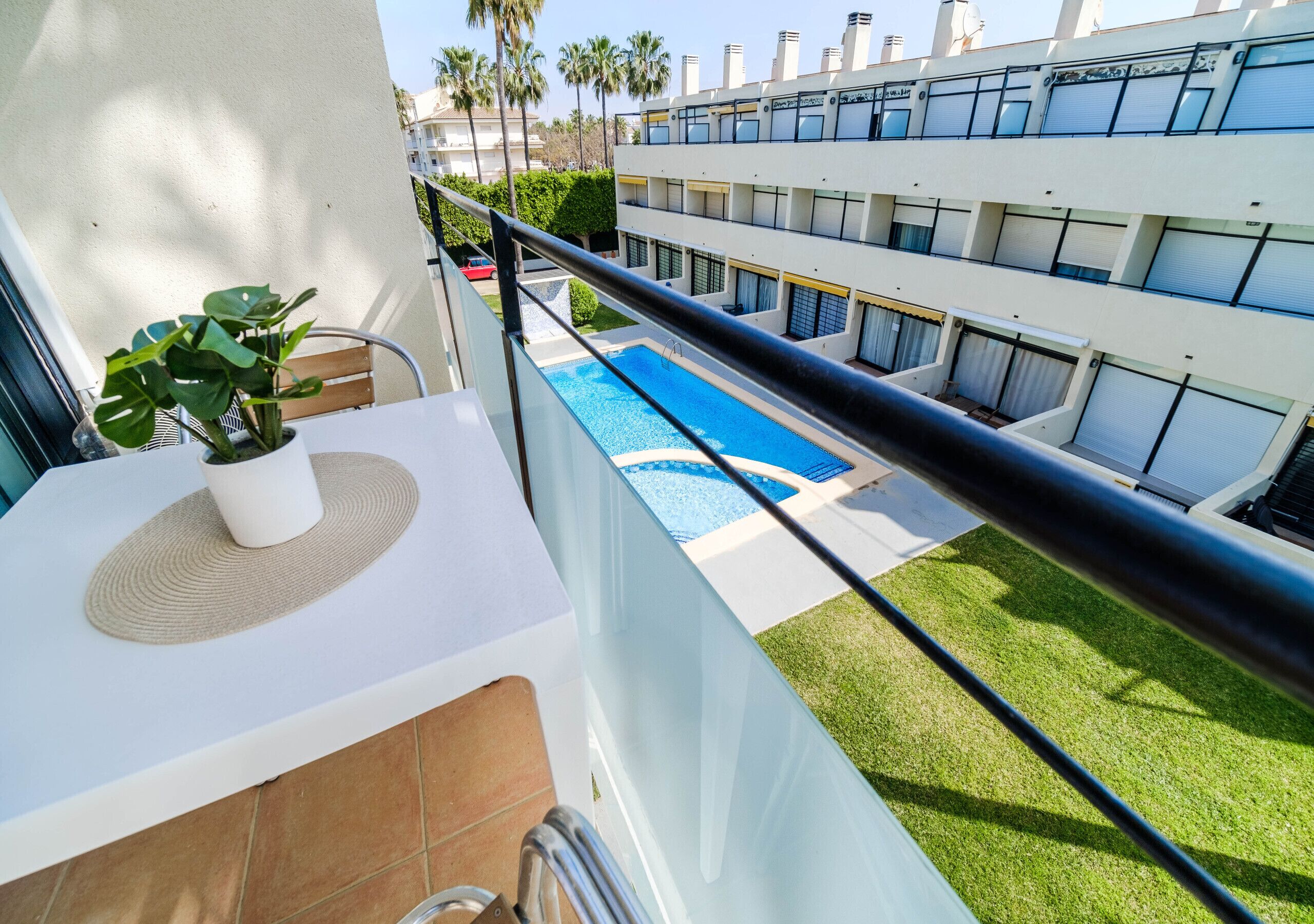 A balcony with a potted plant, a pool, and a building with multiple balconies.