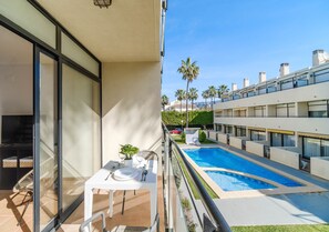 Ein Balkon mit Tisch und Stühlen, ein Schwimmbad und ein Gebäude mit zahlreichen Fenstern und Balkonen.