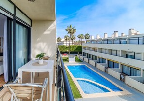 A balcony with a pool, a dining area, and a view of a multi-story building with palm trees. - Santa Barbara Living Apartment Javea (Javea)