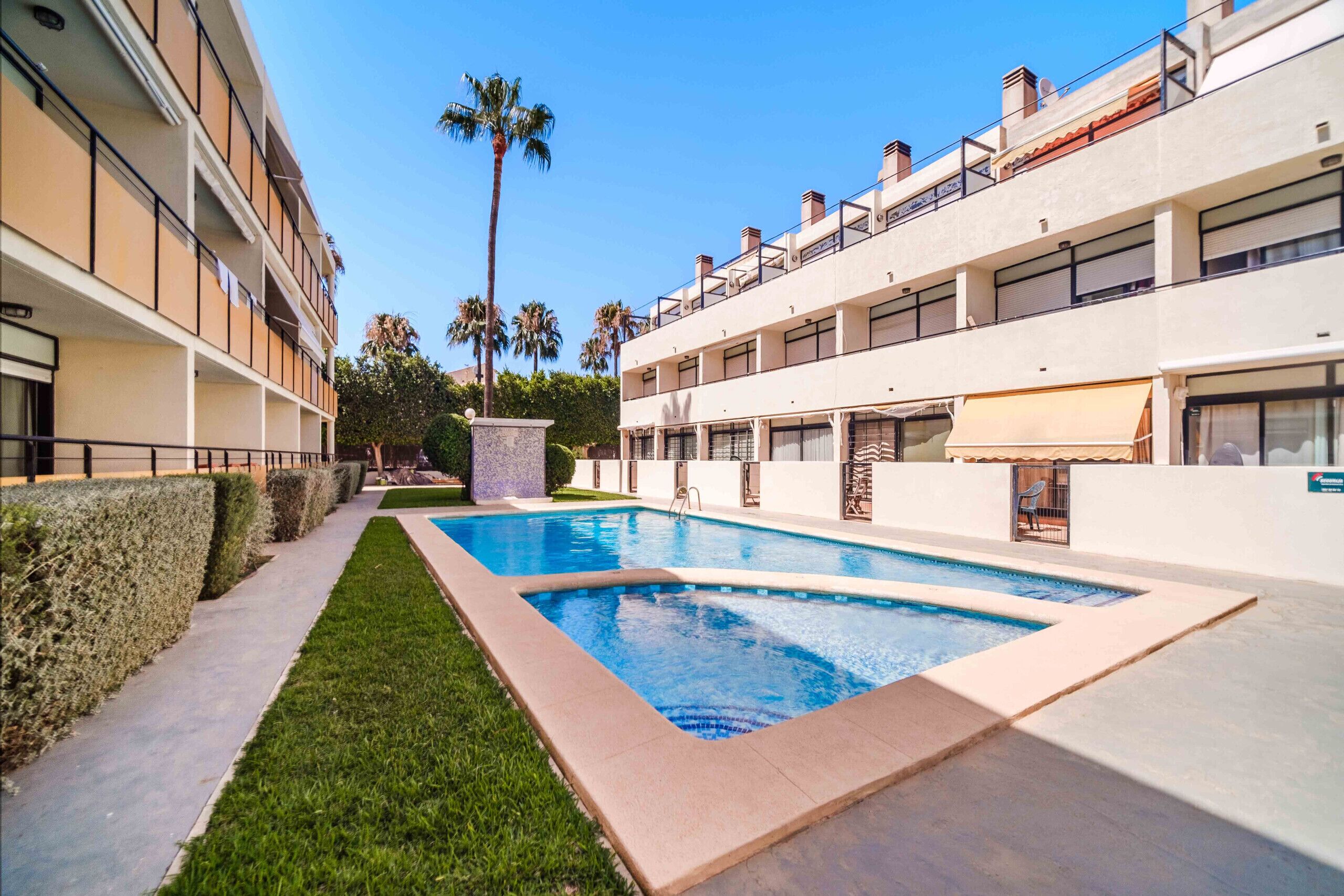 A swimming pool surrounded by a well-maintained lawn and a multi-story building with balconies.