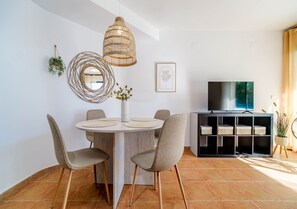 A dining area with a round table, chairs, a hanging light fixture, a television, and a bookshelf. - Santa Barbara Living Apartment Javea (Javea)