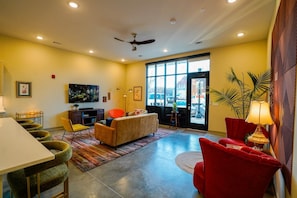 A hotel room with a dining area, a sofa, a red armchair, a television, and a large window with a view. - Opal Suite - NEW 2 bed/2 bath loft near Massachusetts! (Lawrence)