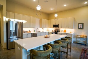 A modern kitchen with a central island, bar stools, stainless steel appliances, and pendant lighting. - Opal Suite - NEW 2 bed/2 bath loft near Massachusetts! (Lawrence)