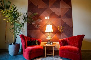 A room with two red armchairs, a small table with a lamp, a large potted plant, and a geometric-patterned wall. - Opal Suite - NEW 2 bed/2 bath loft near Massachusetts! (Lawrence)