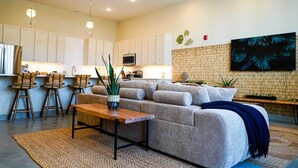 A modern living room with a sofa, a coffee table, and a kitchen area with white cabinets and a microwave.