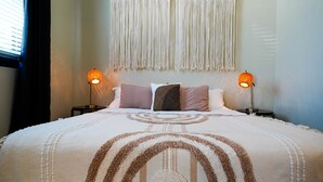 A neatly made bed with a patterned bedspread, two bedside lamps, and a macramé wall hanging.