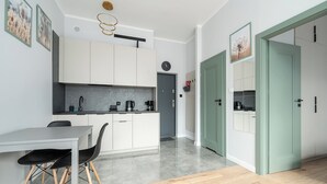 A modern kitchen with white cabinets, a grey countertop, and a dining area with a table and chairs. - RentPlanet - przy Parku Mirowskim (Warsaw)