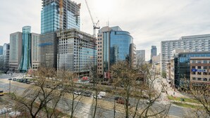 A cityscape with modern buildings, including a construction site and a round building with a blue facade. - RentPlanet - przy Parku Mirowskim (Warsaw)