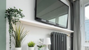 A modern living room with a mounted TV, a radiator, and a wooden console table with potted plants. - RentPlanet - przy Parku Mirowskim (Warsaw)