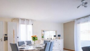 Een eetruimte met een tafel voor vier personen, een wit kastje met spiegel en een deur met raam.