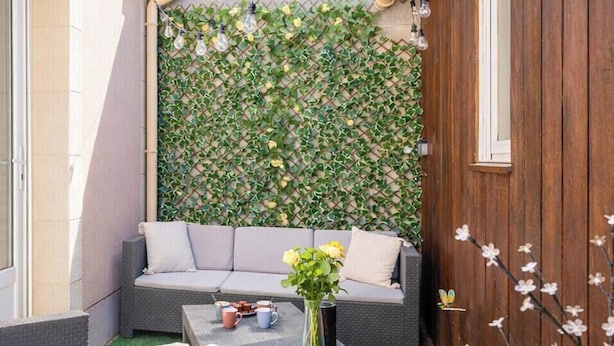 Een zithoek met een comfortabele bank, een klein tafeltje met een bloevas, en een wand begroeid met planten.