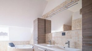 Een moderne badkamer met een grote spiegel, twee wasbakken en een bad.