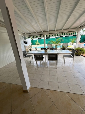 Un patio cubierto con suelo de baldosas, una mesa con sillas y vistas a una piscina.