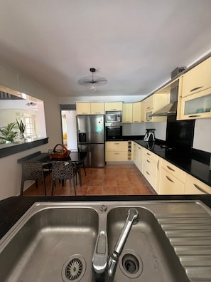 A modern kitchen with stainless steel appliances, a dining area with a table and chairs, and a view of the outside. - VILLA CLIANE (Baie-Mahault)