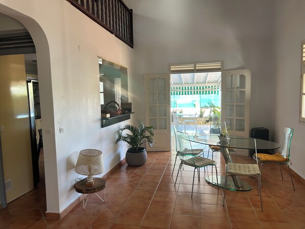 Una habitación amplia con una mesa de cristal, sillas, una planta en maceta y un espejo en la pared.
