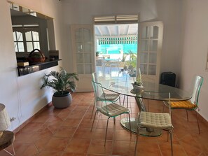 Un área de comedor con una mesa y sillas de vidrio, una planta en maceta y vistas al exterior.